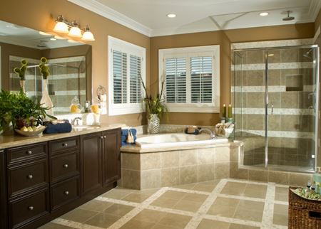 Large remodeled bathroom with large stone tile flooring, separate tub and glass-enclosed shower, dark vanity cabinets, tan walls.