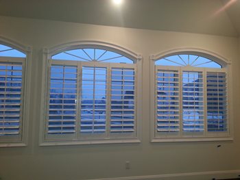 White faux wood blinds on set of three white-framed windows with grids and arched tops.